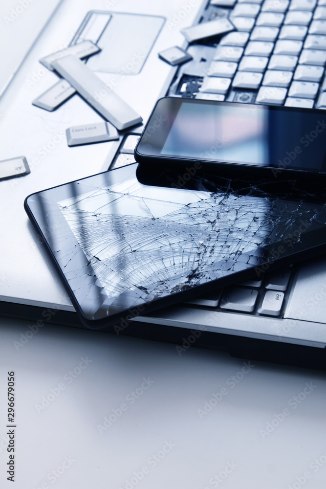 A silver laptop with a broken keyboard, tablet with a cracked display ...