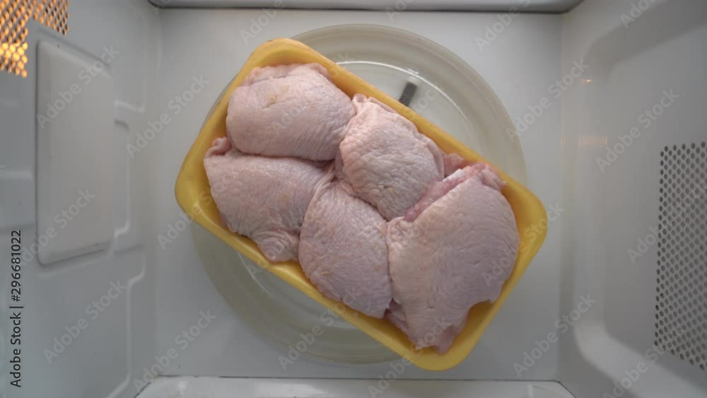 Fresh raw chicken thighs in food tray rotating in microwave top view. Fresh raw chicken thighs in food tray rotating in microwave top view.