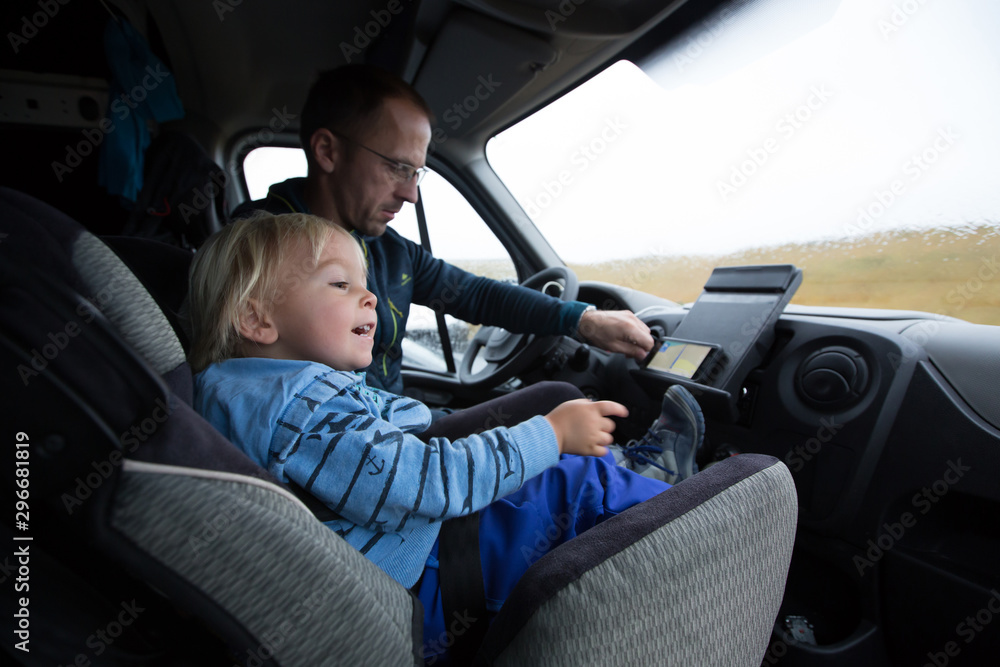 Cute toddler boy, kid sitting on the front seat in child seat on big camper van, smiling