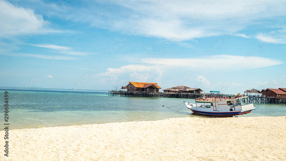 Obraz premium Beautiful view of crystal clear water, white sand, blue sky, traditional cottage, and wooden boat at Derawan Island, Indonesia