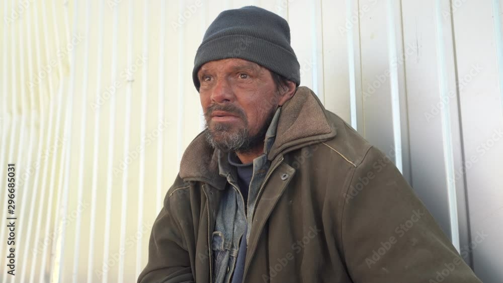 Homeless man sitting on the street near the fence.