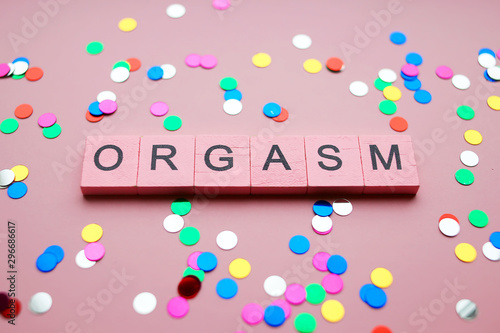 Orgasm wooden words concept on pink background with colored confetti.