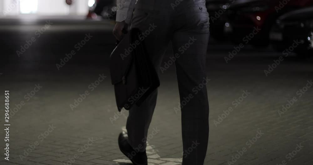 Closeup of a businessman holding a briefcase in his hands and walking in a parking lot.