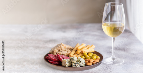 Glass of White wine and wood plate with antipasti. Blue cheese, olives, baguette slices, dry cured sausages and nuts. Wine snacks set background for banner