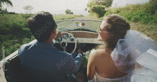 Happy diverse newly wed couple driving on a country road, bride and groom driving together in a vintage convertible