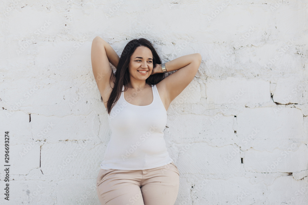 Plus size model dressed in white shirt posing over brick wall