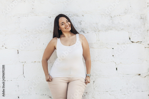 Plus size model dressed in white shirt posing over brick wall photo