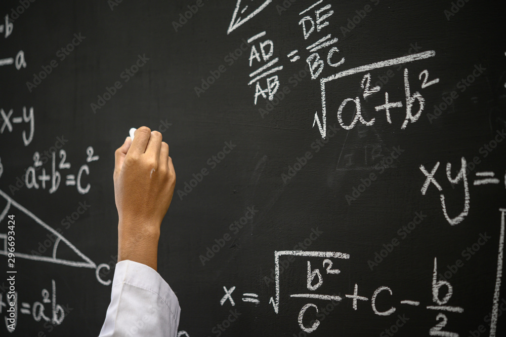 The hand that writes the formula with white chalk on the blackboard
