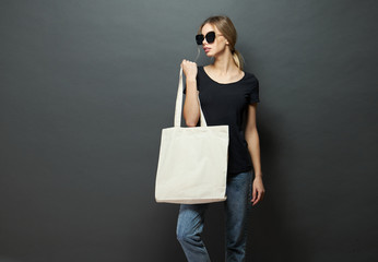 Young woman holding white textile eco bag against gray background. Ecology or environment protection concept. White eco bag for mock up.