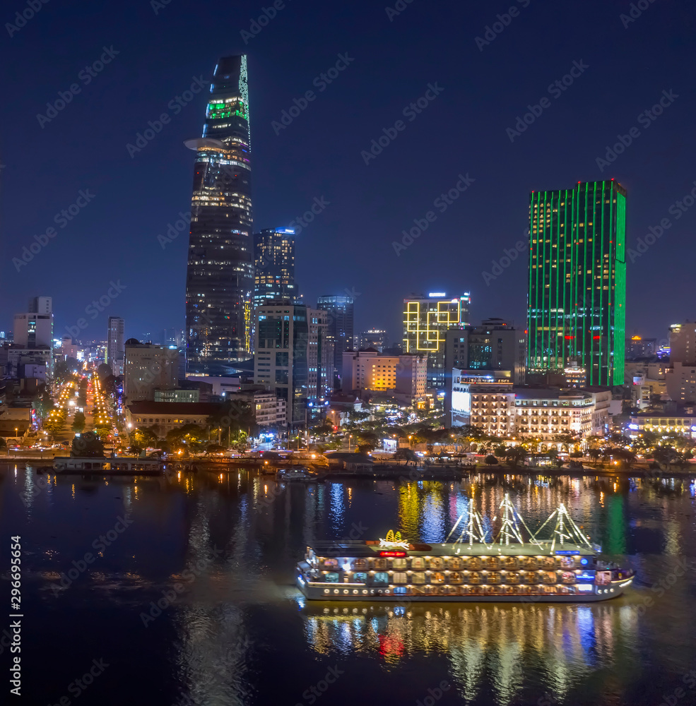 Classic night skyline under full lights of Ho Chi Minh City with Saigon river and large tourist boat