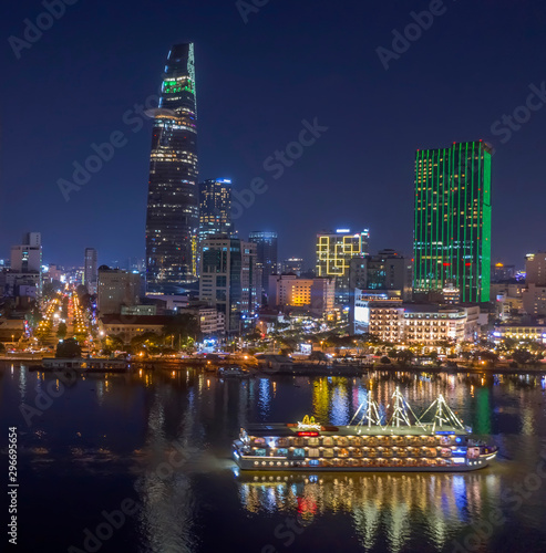 Classic night skyline under full lights of Ho Chi Minh City with Saigon river and large tourist boat