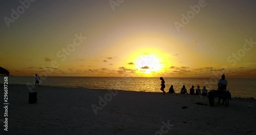 group of tourists enjoying golden sunset on tropical sandy beach while one man is running on the sand. Drone parallax shot photo