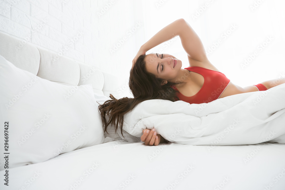 young attractive woman in red sexy underwear touches her long brown hair lying in bed in bright bedroom young attractive woman in red sexy underwear touches her long brown hair lying in bed in bright bedroom