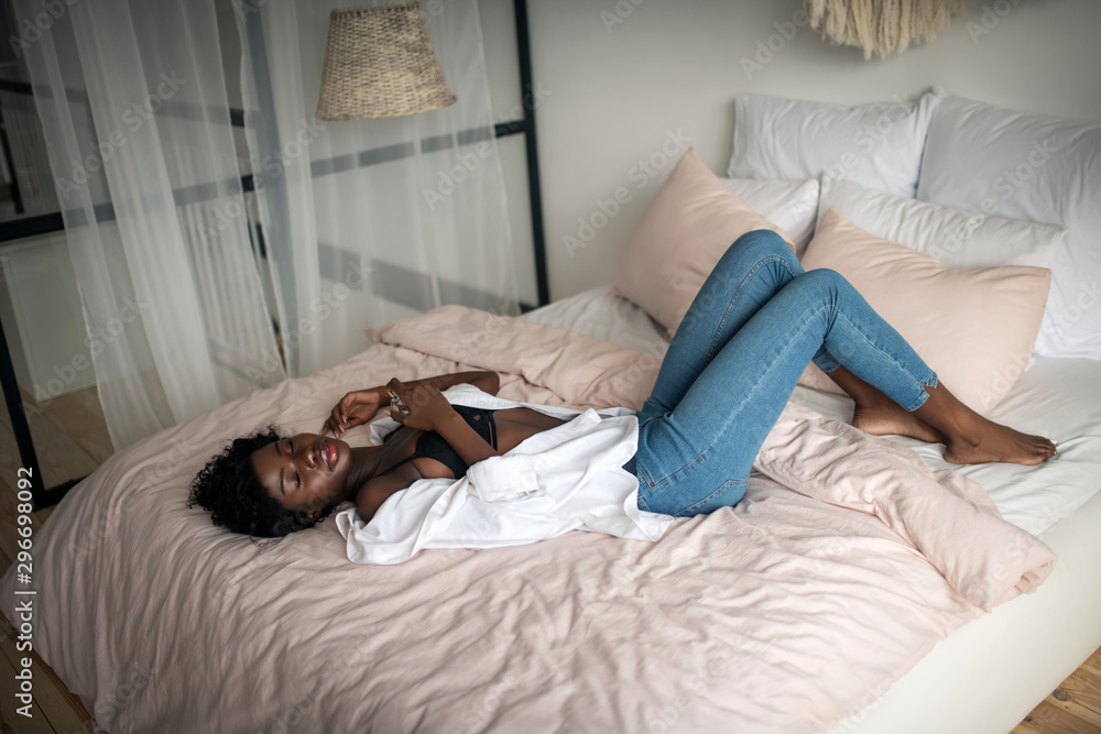 Obraz premium Woman wearing jeans and black bra chilling on bed