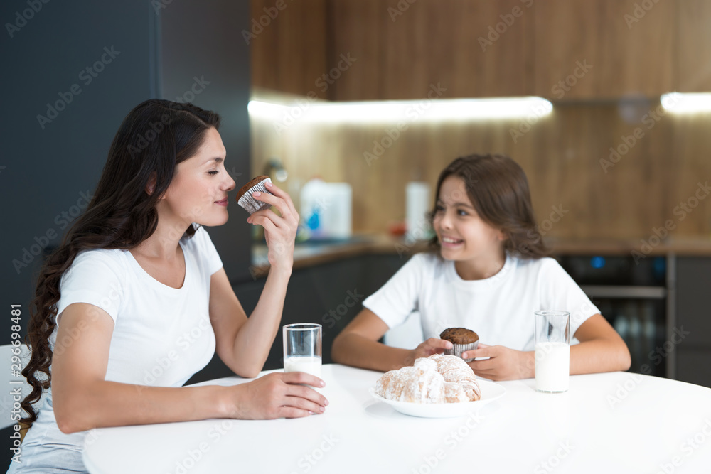 beautiful young mother with her cute teenager daughter eating cupcakes and croissants for breakfast in the kitchen looking happy beautiful young mother with her cute teenager daughter eating cupcakes and croissants for breakfast in the kitchen looking happy