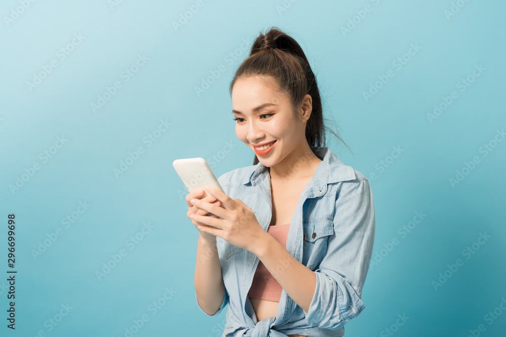 Asian woman 20s holding mobile phone and smiling over blue background Asian woman 20s holding mobile phone and smiling over blue background