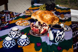 Traditional Uzbek bread on table with mugs and kettle. Cuisine of Central Asia. fruits grapes and pomegranate and sweets in plates
