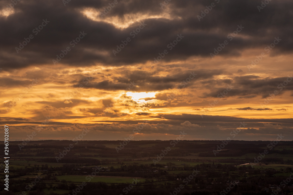 The sun sets through dramatic clouds that loom over horizon overlooking the English countryside. The sun sets through dramatic clouds that loom over horizon overlooking the English countryside.