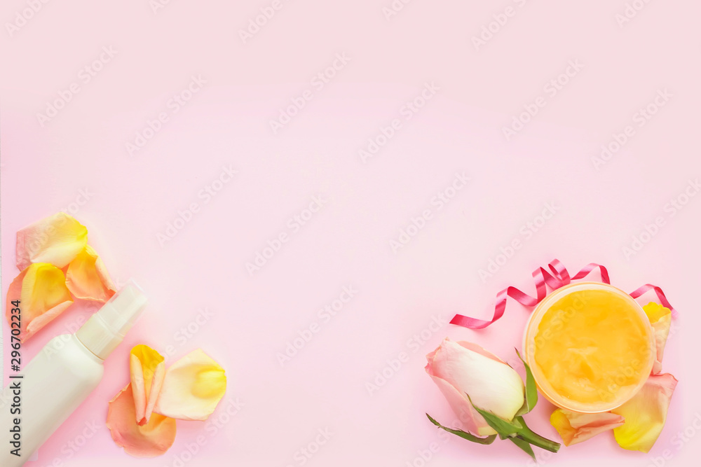 Open jar of cosmetic cream, white cosmetics bottle, rose and rose petals on pink background. Concept of natural spa cosmetics. Flat lay, top view, copy space.