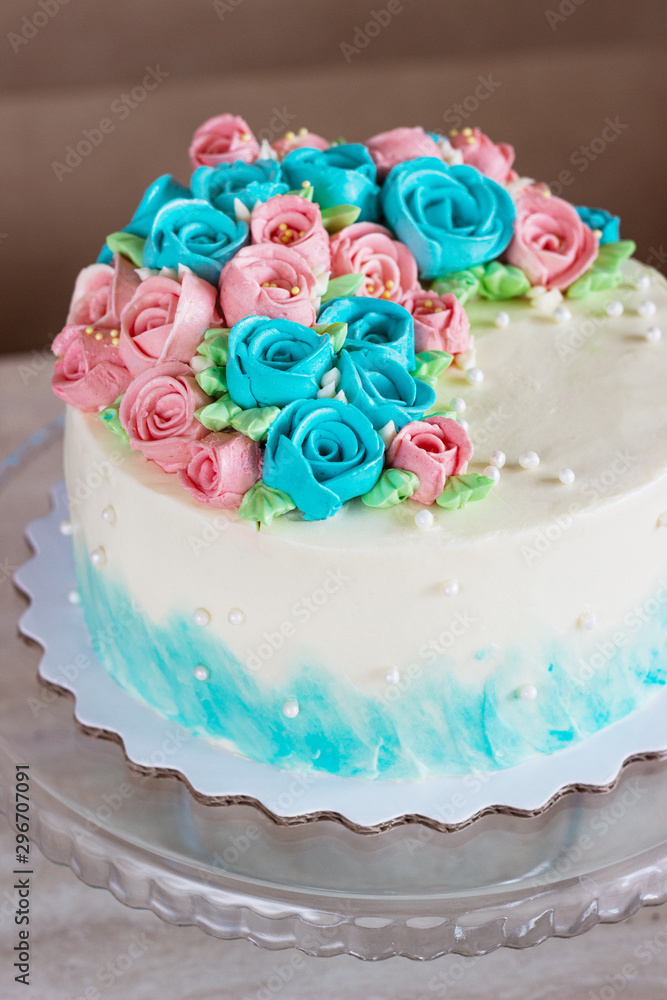 Gorgeous cake covered in bright roses made of butter cream icing on light wooden background Gorgeous cake covered in bright roses made of butter cream icing on light wooden background