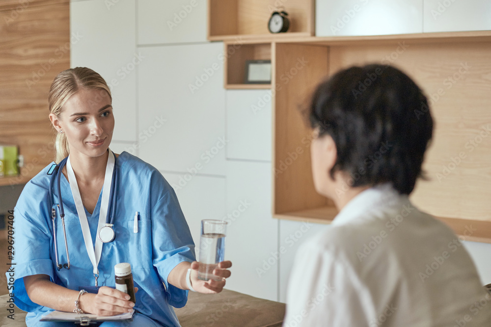 Obraz premium Beautiful smiling woman the doctor in a bottle of pill offers the patient