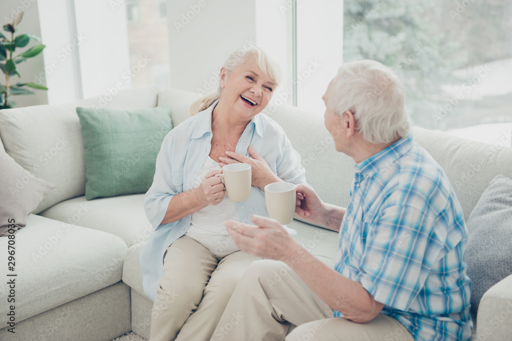 Photo of two pretty aged people excited pair laughter communicating tea mugs hands comfortable flat sitting sofa indoors - obrazy, fototapety, plakaty 