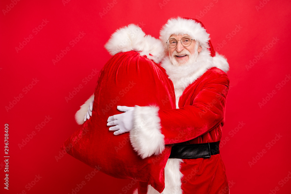 Portrait of his he nice glad cheerful cheery bearded Santa wearing fur coat carrying holding in hands sack holly jolly December night isolated over bright vivid shine vibrant red background Portrait of his he nice glad cheerful cheery bearded Santa wearing fur coat carrying holding in hands sack holly jolly December night isolated over bright vivid shine vibrant red background