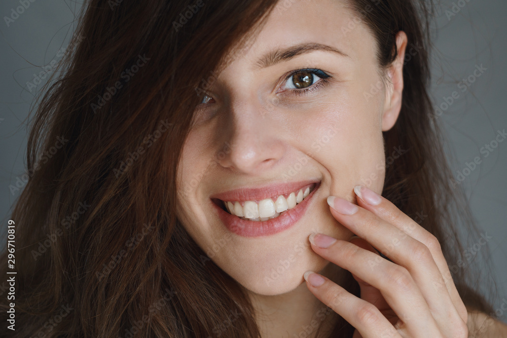 Close picture of a young woman smiling and touching her glowing smooth face Close picture of a young woman smiling and touching her glowing smooth face