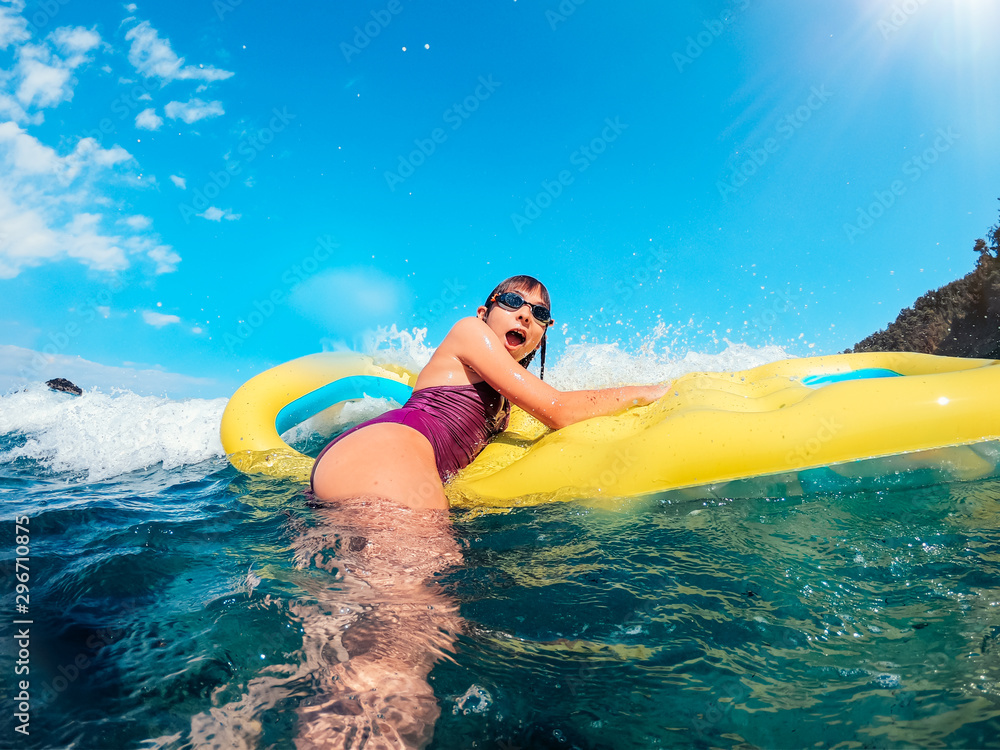 Excited girl floating on the yellow inflatable airbed in the sea