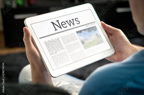 Man reading the news on tablet at home. Imaginary online and mobile news website, application or portal on modern touch screen display. Holding smart device in hand. photo