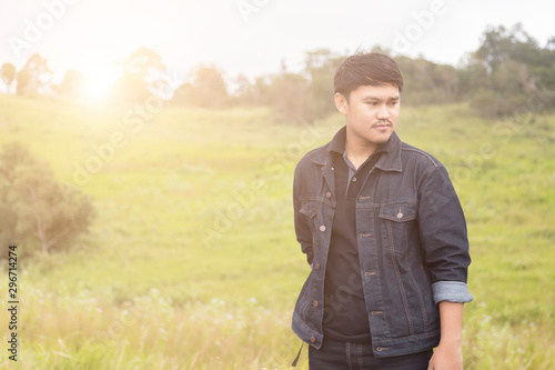 Portrait of asian man are standing on road  with blurred of grass field on the background. Man in a black shirt standing and enjoying the beautiful nature. © witsawat