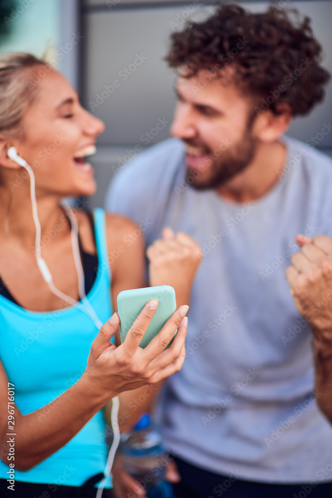 Modern woman and man jogging / exercising in urban surroundings and using cellphone at a pause / break.