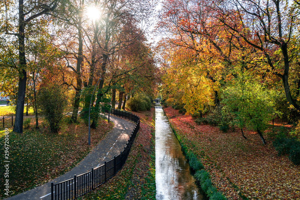 River and bicycle path in the city park in autumn. Sun rays shining through the branches of trees. Bialystok in Poland. Europe River and bicycle path in the city park in autumn. Sun rays shining through the branches of trees. Bialystok in Poland. Europe