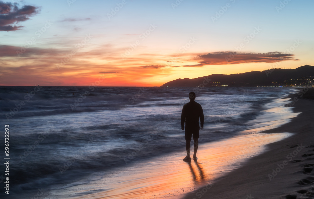 Silhouette of a man standing in sea landscape with dramatic sunset sky