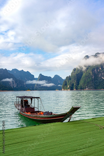 Wooden boat in lake with mountain range and clouds background © oppdowngalon