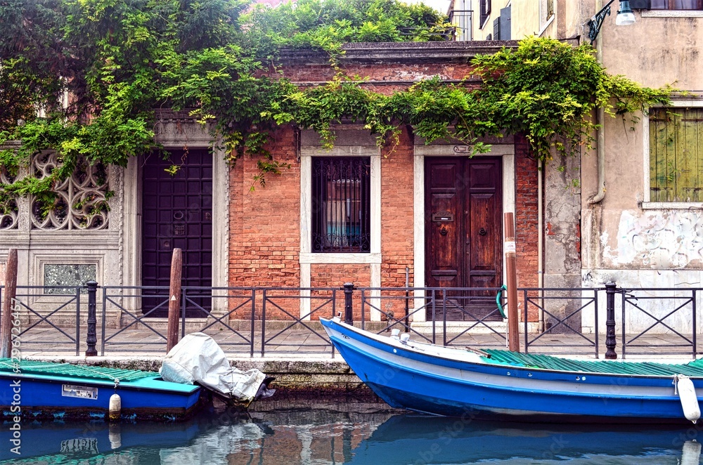 Venetian pedestrian street along the canal with boats and houses Venetian pedestrian street along the canal with boats and houses