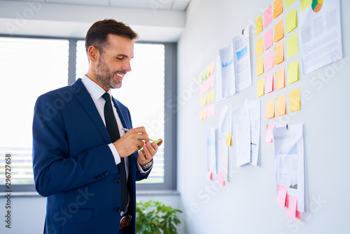 Smiling businessman writing a note to post on office wall