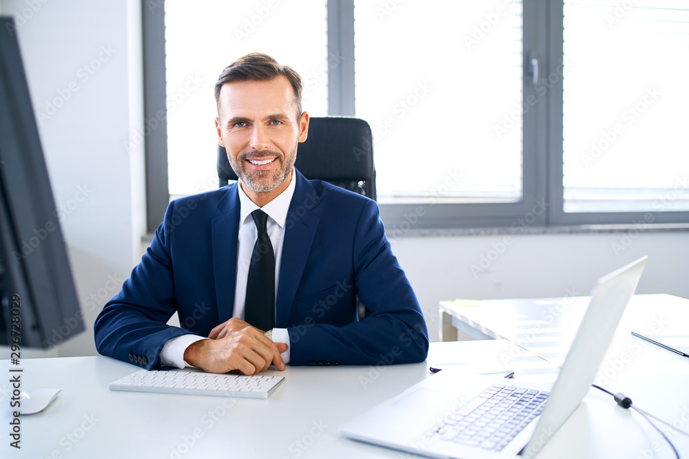 Portrait of smiling businessman sitting in office and looking at camera Portrait of smiling businessman sitting in office and looking at camera