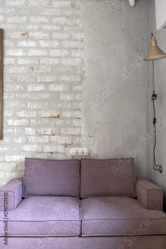 Comfortable pink soft couch with velour upholstery standing against white brick and plastered wall in light loft apartment in daytime