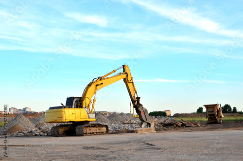 Excavator on a construction site cuts and crumbles old concrete and asphalt. Hydraulic breaker grinder. Crusher for concrete slabs. hydraulic shears  Hammer crushes 