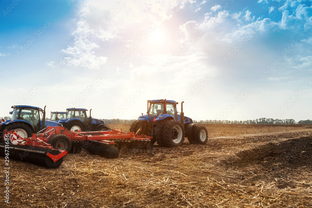 Obraz premium Several tractors plows the field, cultivates the soil for sowing grain. The concept of agriculture and agricultural machinery.