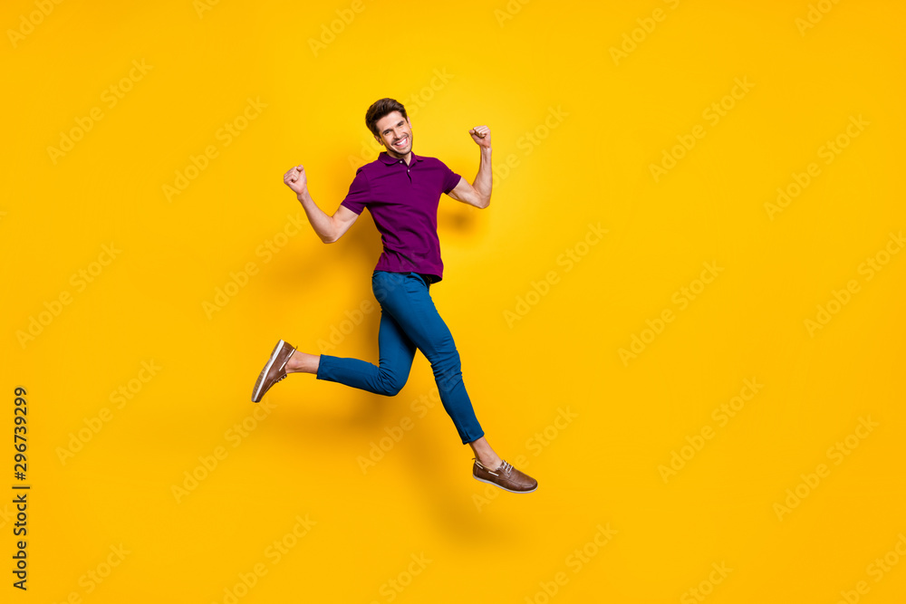 Full length body size photo of cheerful positive strong man running jumping demonstrating his powerful muscles wearing blue pants trousers purple t-shirt isolated over vivid color background