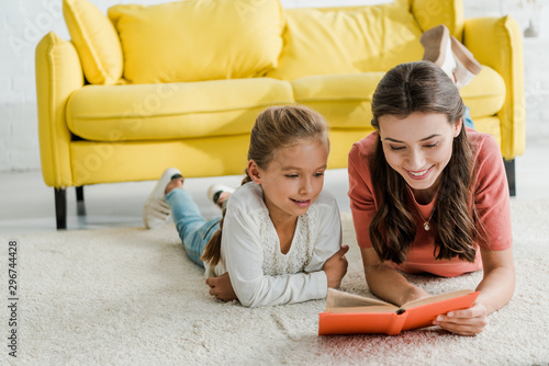 happy babysitter lying on carpet with smiling kid while reading book