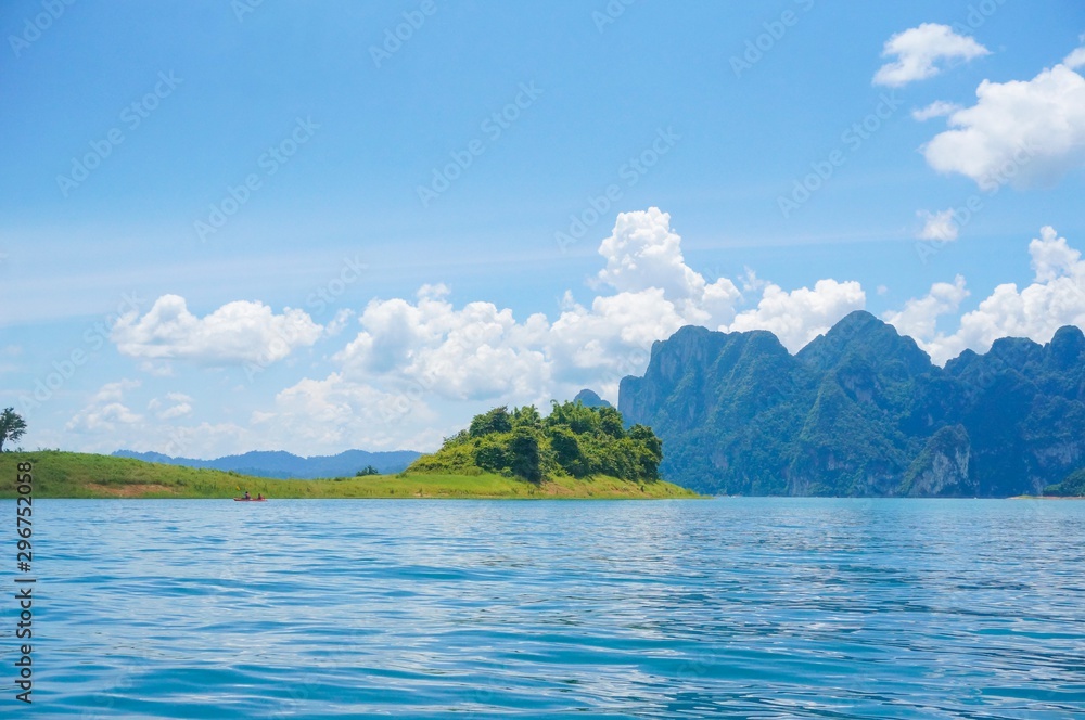 Fototapeta premium Beautiful view from Ratchaprapa dam in Thailand. Beautiful landscape view with blue water, blue clouds sky and mountains at the background. Tourists in the boat are enjoying the view