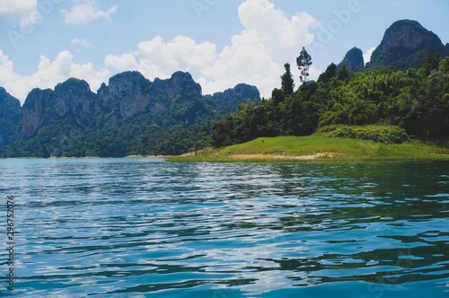 Beautiful view from Ratchaprapa dam in Thailand. Beautiful landscape view with blue water, blue clouds sky and mountains at the background. Tourists in the boat are enjoying the view © yaangsgap
