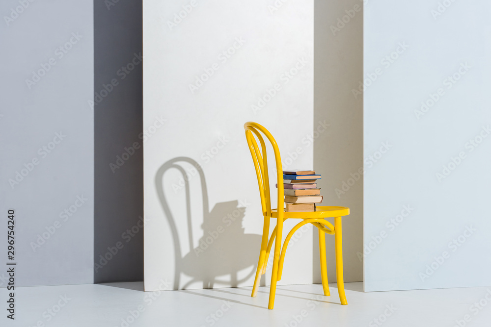 Fototapeta premium books on yellow chair on white and grey with copy space