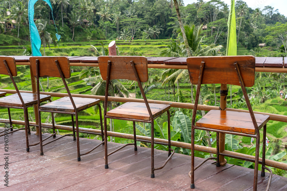 Wooden table and chairs in empty tropical cafe next to rice terraces in island Bali, Indonesia