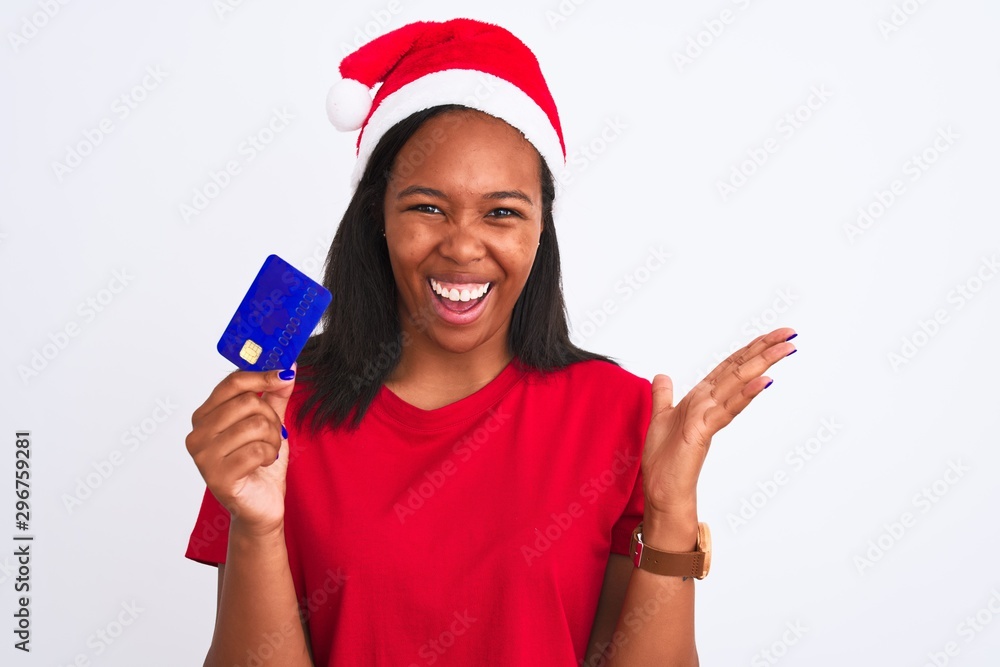 Young african american woman wearing christmas hat and holding credit card very happy and excited, winner expression celebrating victory screaming with big smile and raised hands Young african american woman wearing christmas hat and holding credit card very happy and excited, winner expression celebrating victory screaming with big smile and raised hands