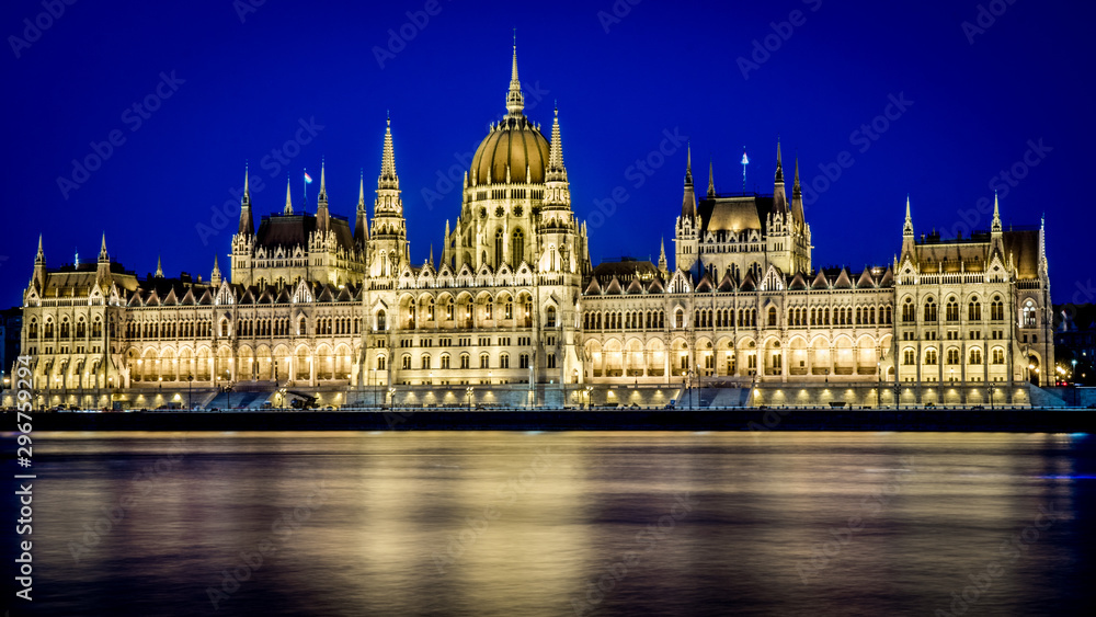 Illuminated Hungarian Parliament at night with yellow light and water reflection. Budapest, Hungary.