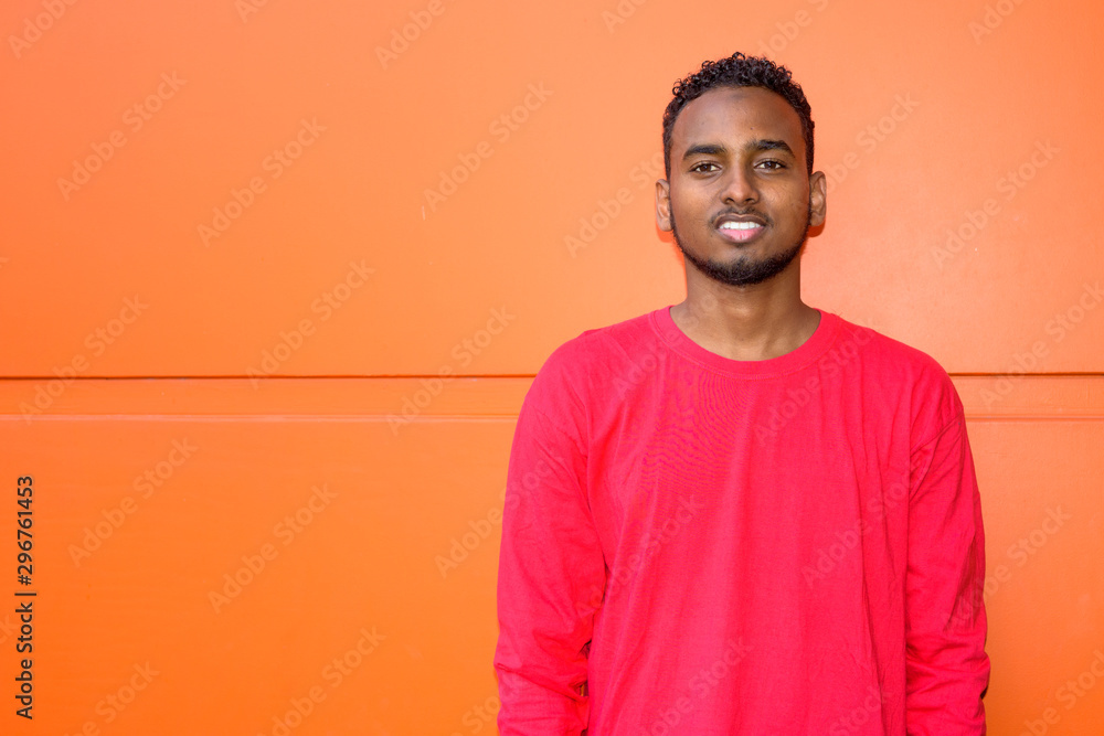 Face of happy young African bearded man smiling against orange wall Face of happy young African bearded man smiling against orange wall
